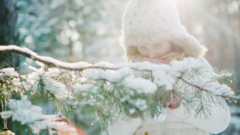 the little girl in a warm knitted hat prepares for christmas decorates the new year tree with colorf