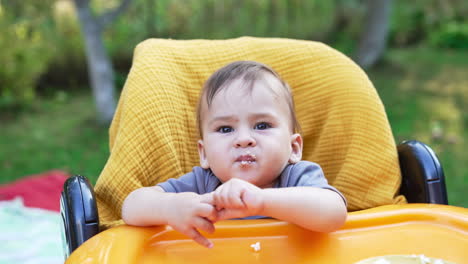 lovely baby doesn't want to eat. mommy tries to feed her kid with cottage cheese but little turns his head away. close up. outdoors.