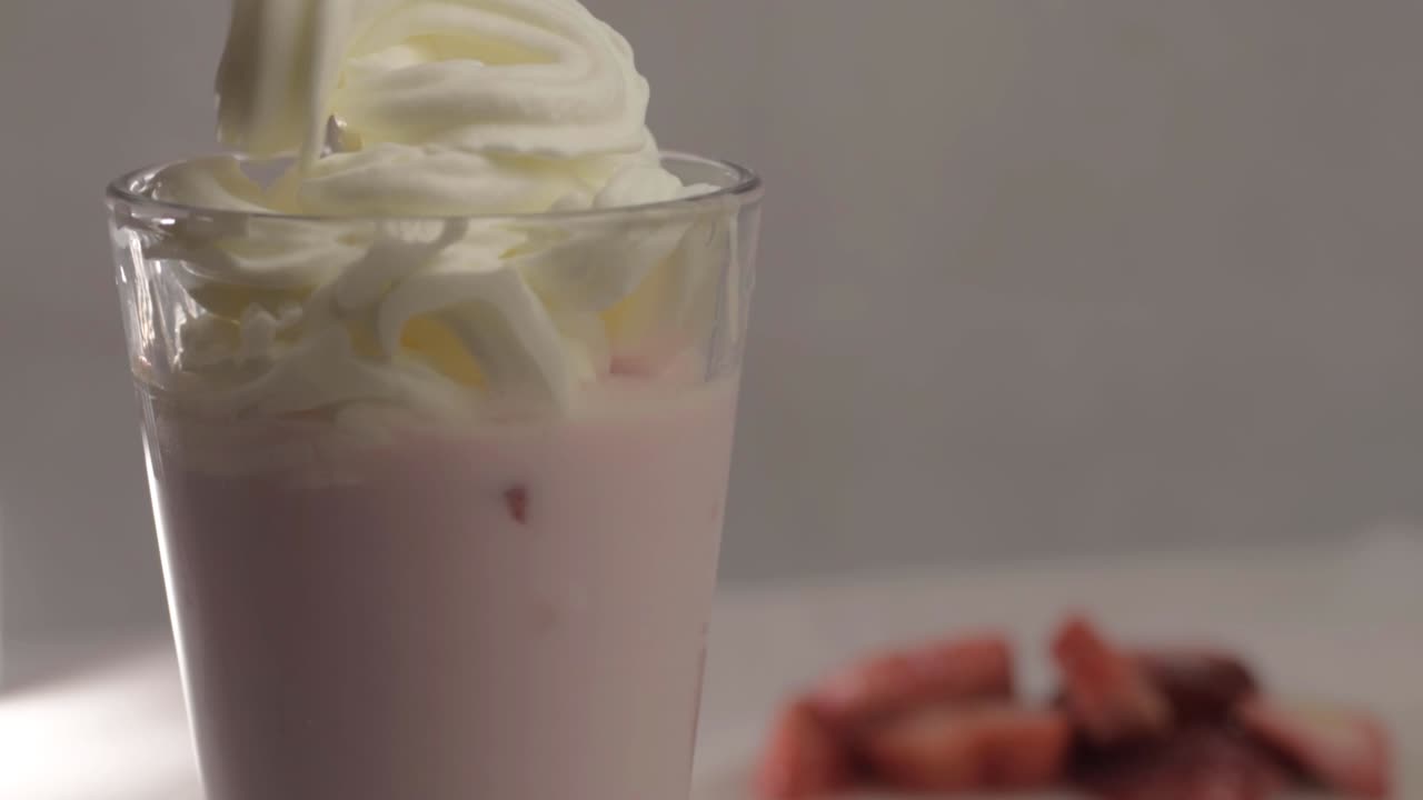 Hand pouring whipped cream topping on strawberry milkshake close up shot