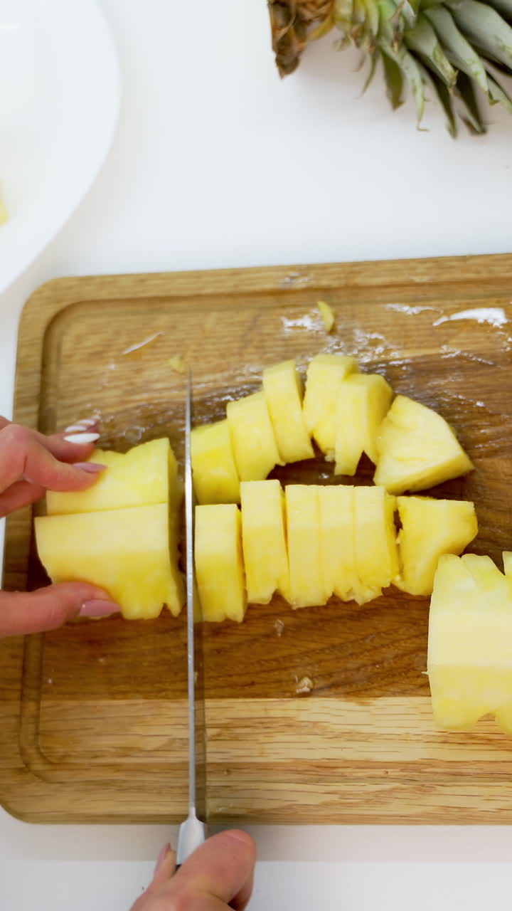 Sliced pieces of pineapple. Peeled pineapple woman cutting into pieces on a wooden board. Tropical food concept. Vertical video