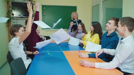 teen students at school. happy children sitting in the classroom and throw papers up. students enjoys the time together. papers flying in the class. slow motion.