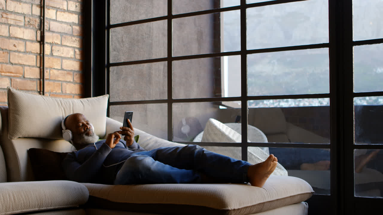 hombre mayor escuchando música en el teléfono móvil en la sala de estar 4k