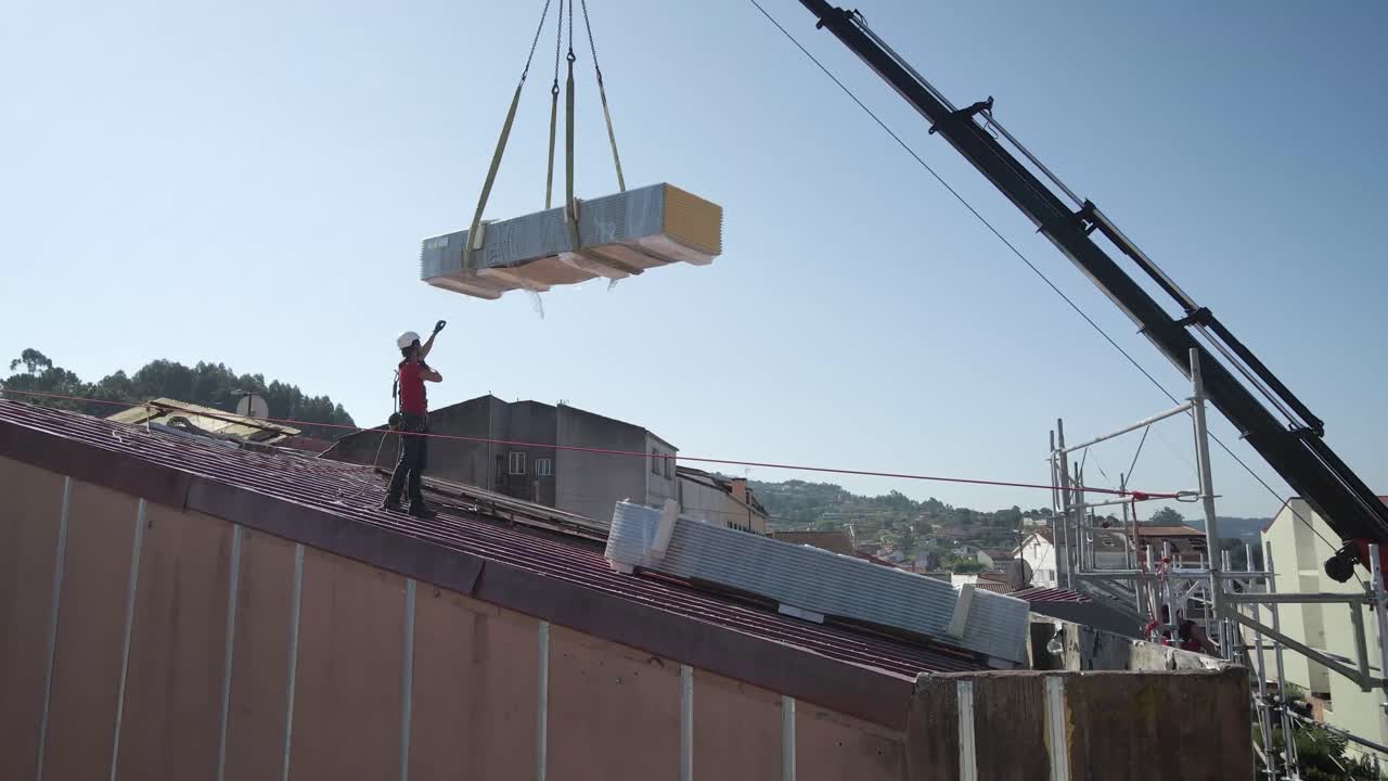 Worker at a construction roof directing a load to be downloaded