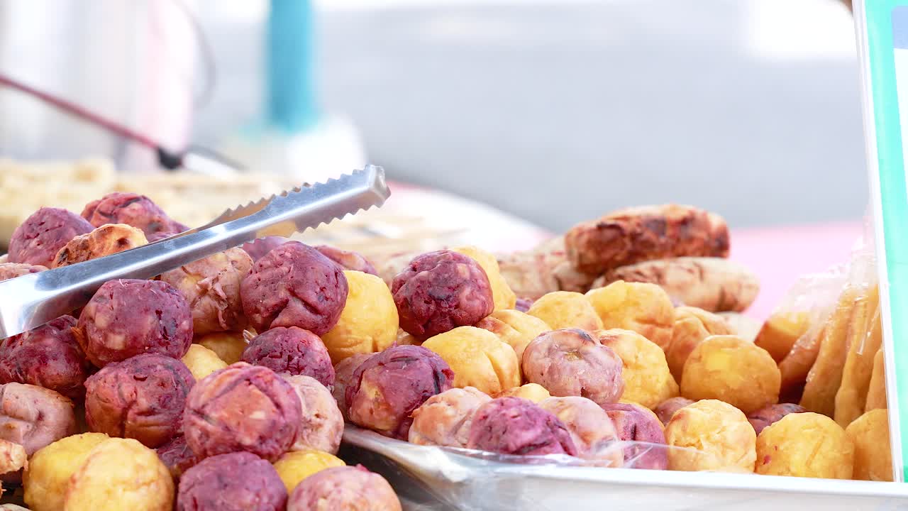 Close-up of vibrant grilled taro balls at a bustling Phuket street market. Bright lighting highlights the colorful display