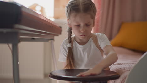 Girl-in-t-shirt-plays-with-stool-by-electric-piano-at-home