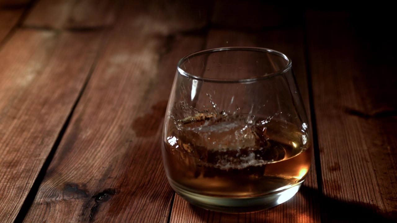 Caduta al rallentatore di un cubetto di ghiaccio in un bicchiere di whisky