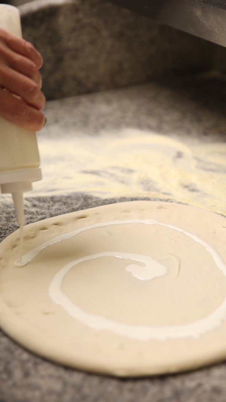 Hand Squeezing White Sauce onto Raw Pizza Dough