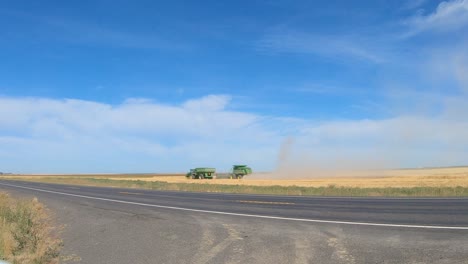combine harvester and grain wagon are harvesting wheat in eastern washington state with traffic passing in the foreground