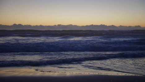 Waves-of-the-Pacific-Ocean-gently-roll-in-after-sunset,-their-rhythmic-motion-reflecting-the-fading-light-and-creating-a-serene,-calming-ambiance-on-the-tranquil-evening-sea