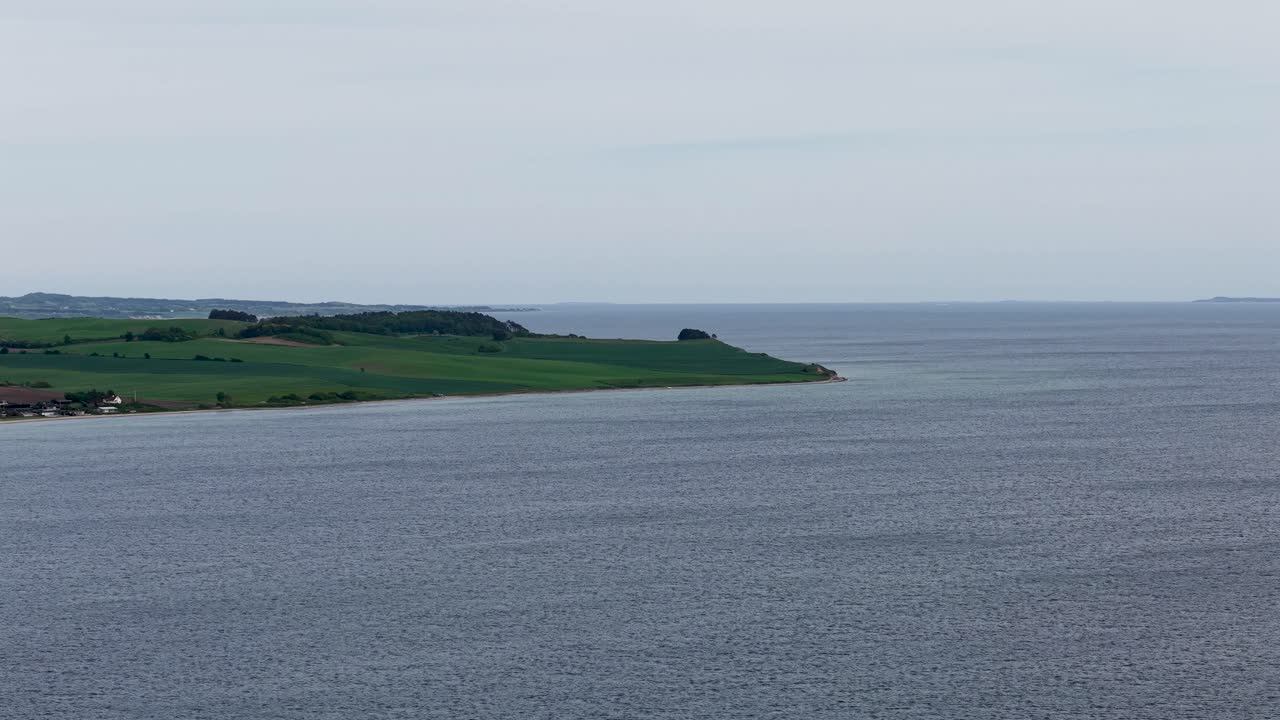 Aerial view of calm coastal waters meeting the green, rolling shoreline of Mols Bjerge National Park in Denmark