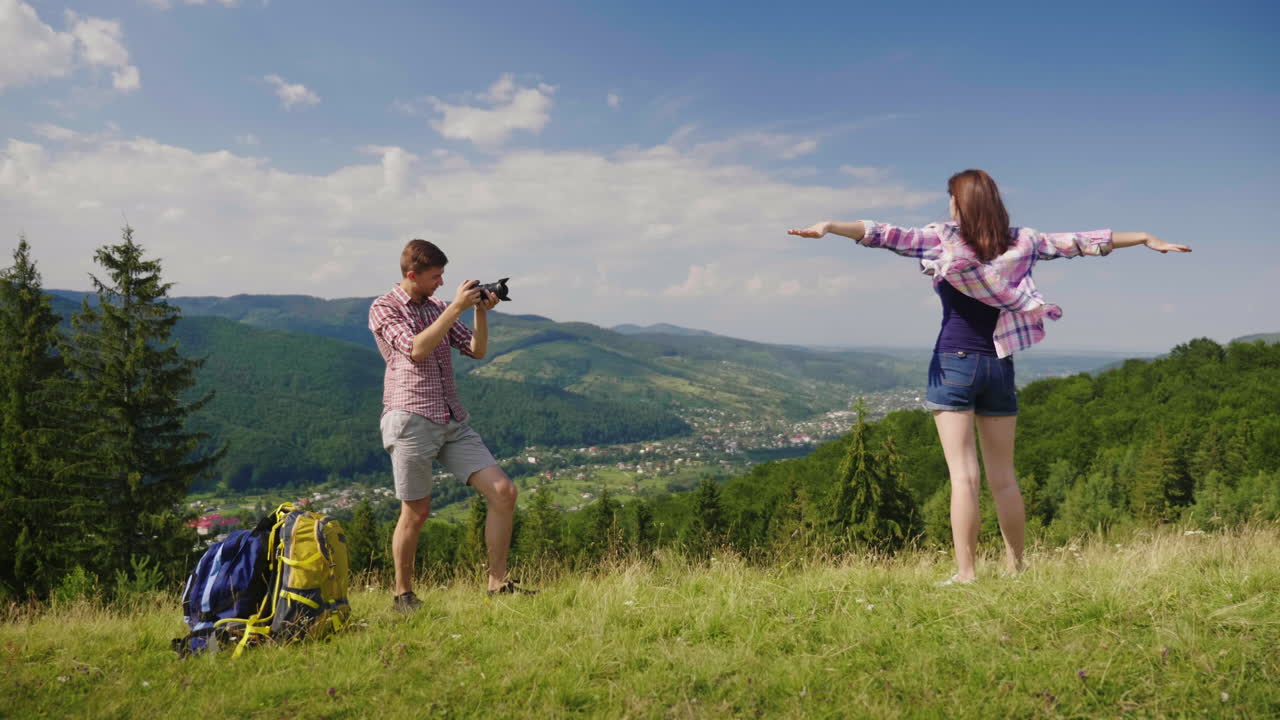 그 남자는 산을 배경으로 한 그림 같은 곳에서 여자 친구의 사진을 찍는다.