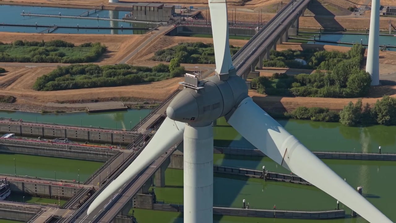 Aerial shot of a large wind turbine generating clean energy, with the krammersluizen locks and a highway bridge in the background