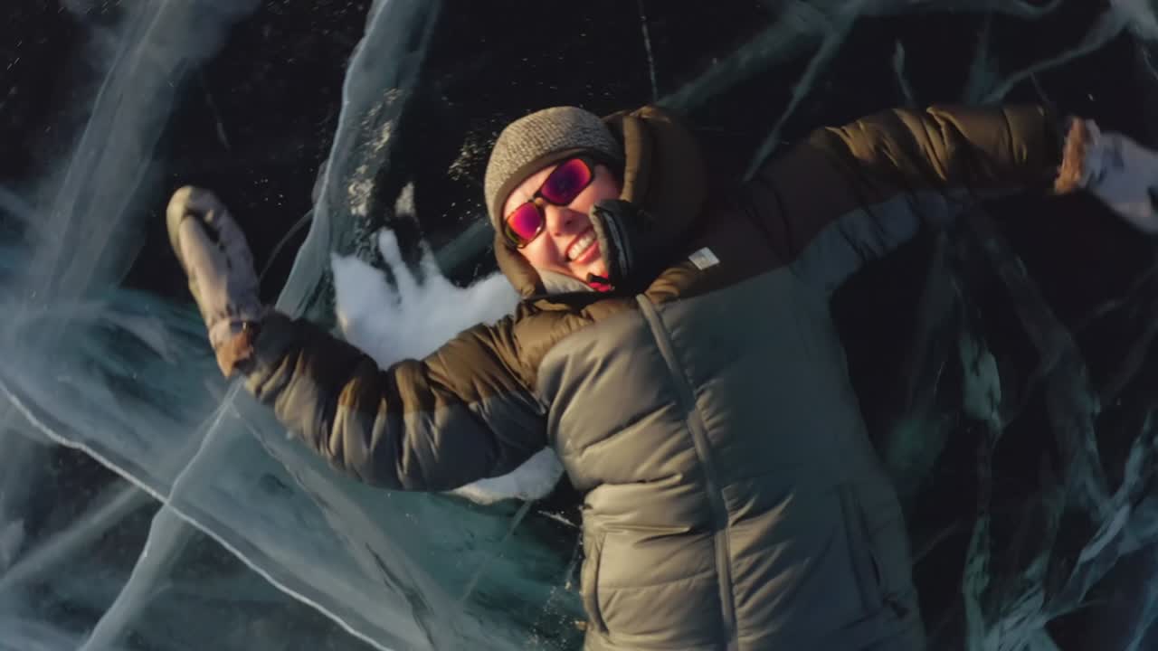 девушка лежит на льду зимой, размахивая руками и ногами в сторону, изображая ангела.