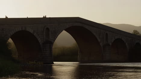 stone arch bridge with people silhouetted at sunset over a river