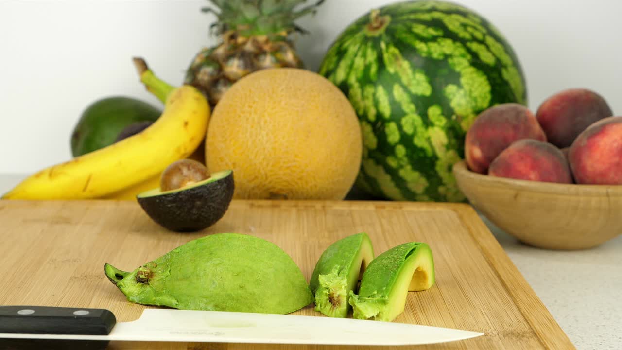toma de seguimiento de un aguacate en rodajas en una tabla de corte, frente a varios trozos de fruta y un fondo blanco simple