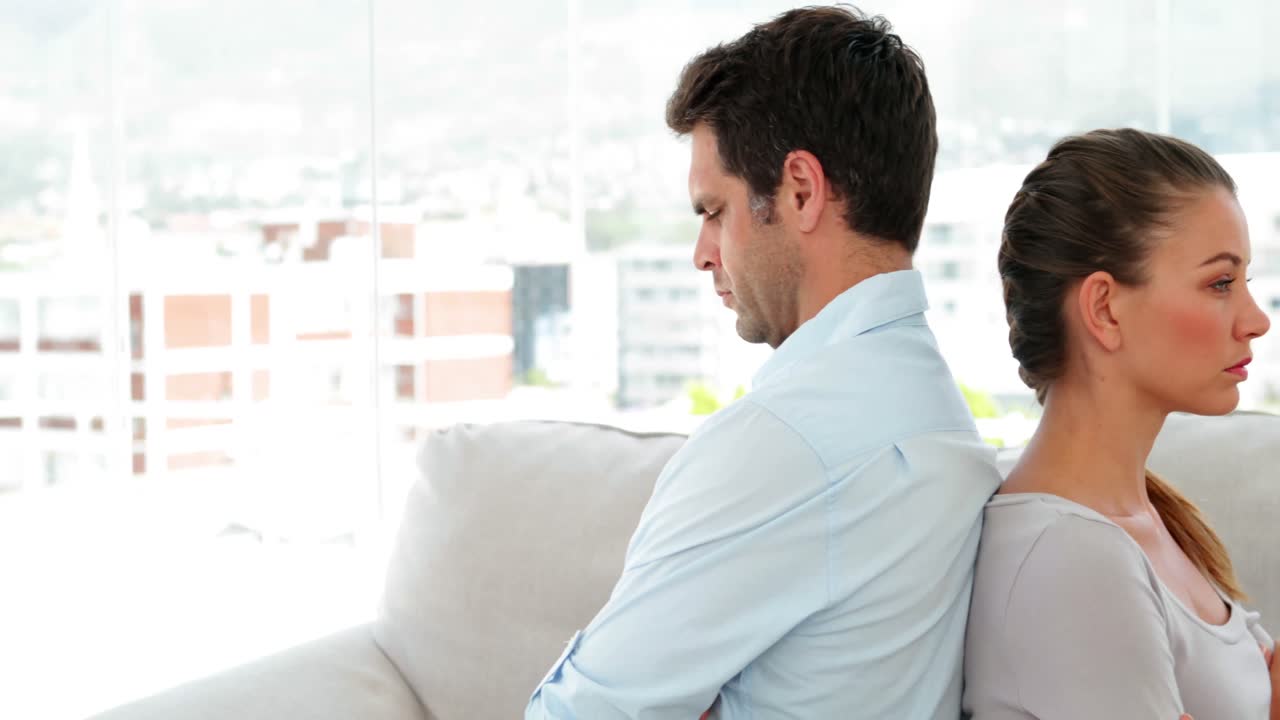 pareja sentada espalda con espalda después de una pelea en el sofá