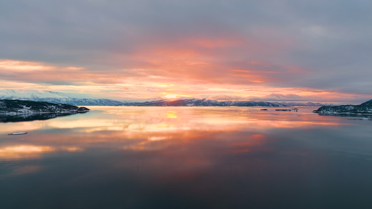 Splendida vista aerea di un tramonto dorato che si riflette sulle acque calme di un fiordo norvegese nell'arcipelago delle Lofoten durante l'inverno