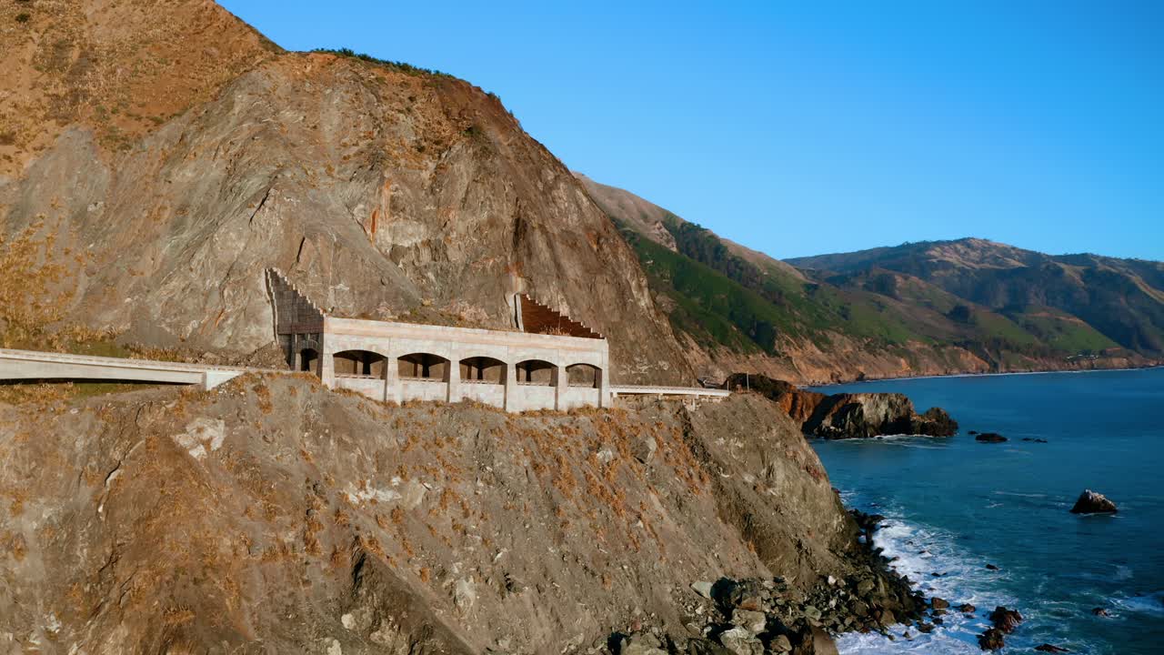 A car passes through the Rain Rocks Rock shed with ocean waves crashing along the shoreline below