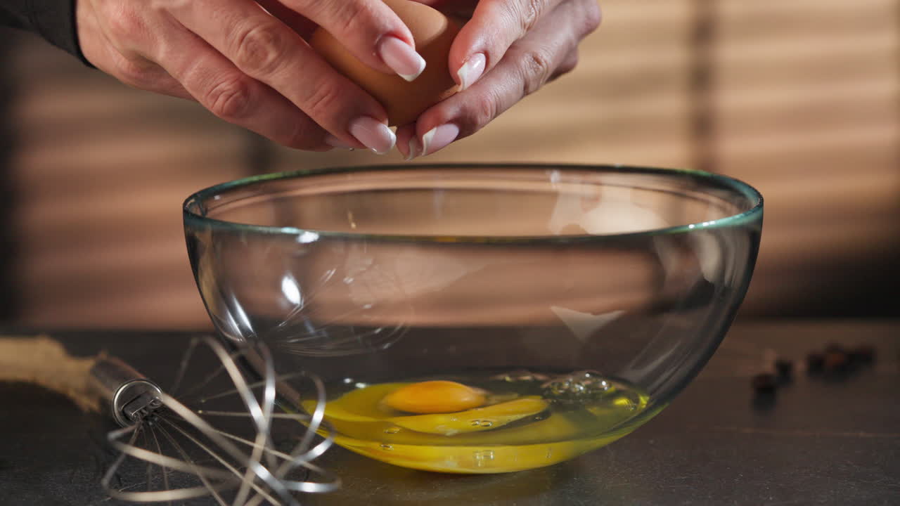 Static shot of woman's hands breaking an egg and pouring it into a bowl for a tiramisu, interior