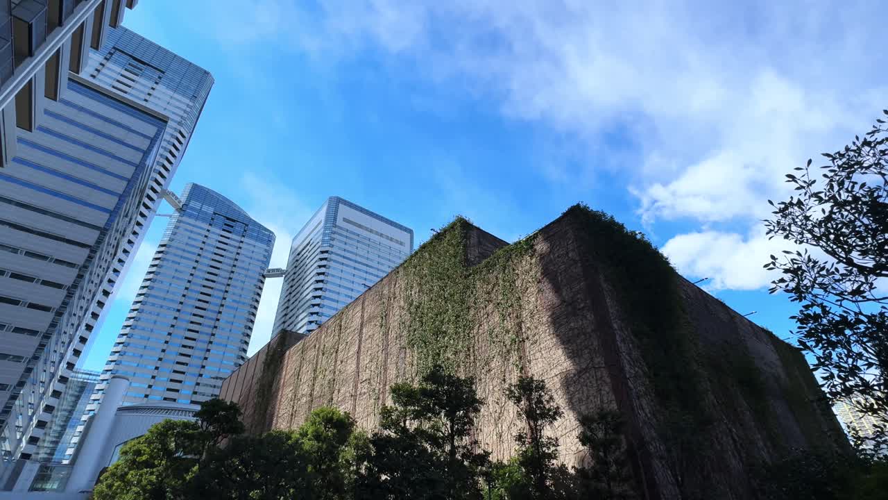 Urban skyline with tall buildings, green-covered wall, and bright blue sky in Harumi