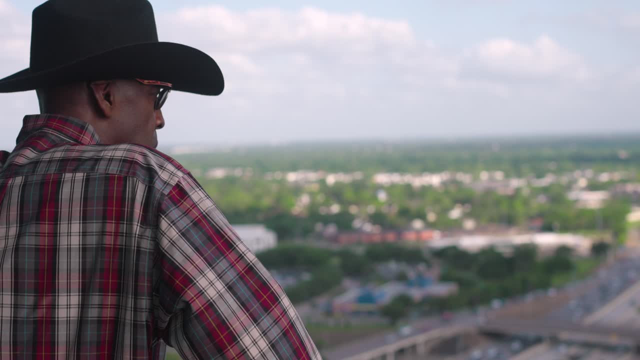 Uomo nero con cappello da cowboy che si affaccia dal balcone.