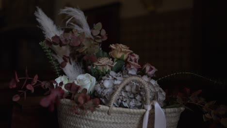 Rustic-basket-with-roses,-greenery,-and-pampas-grass-in-a-dimly-lit-setting