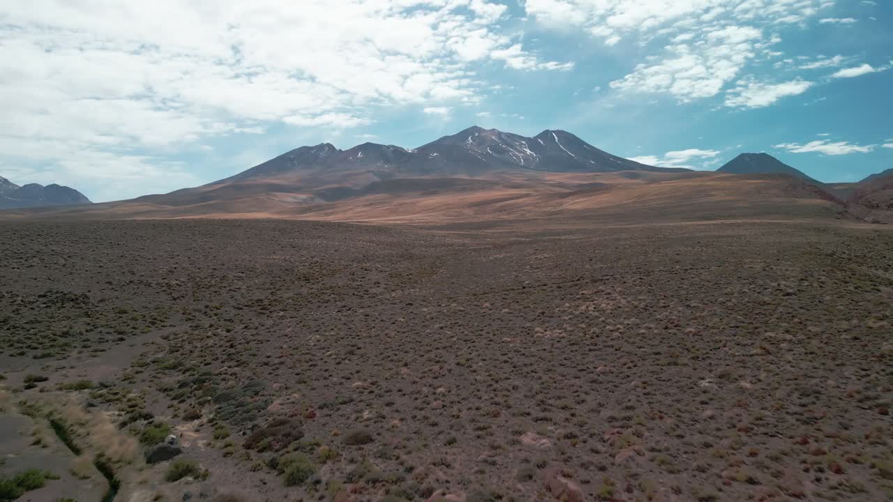 rodaje de drones yendo a un volcán en el desierto chileno pasando cerca de la vegetación seca que está en el suelo