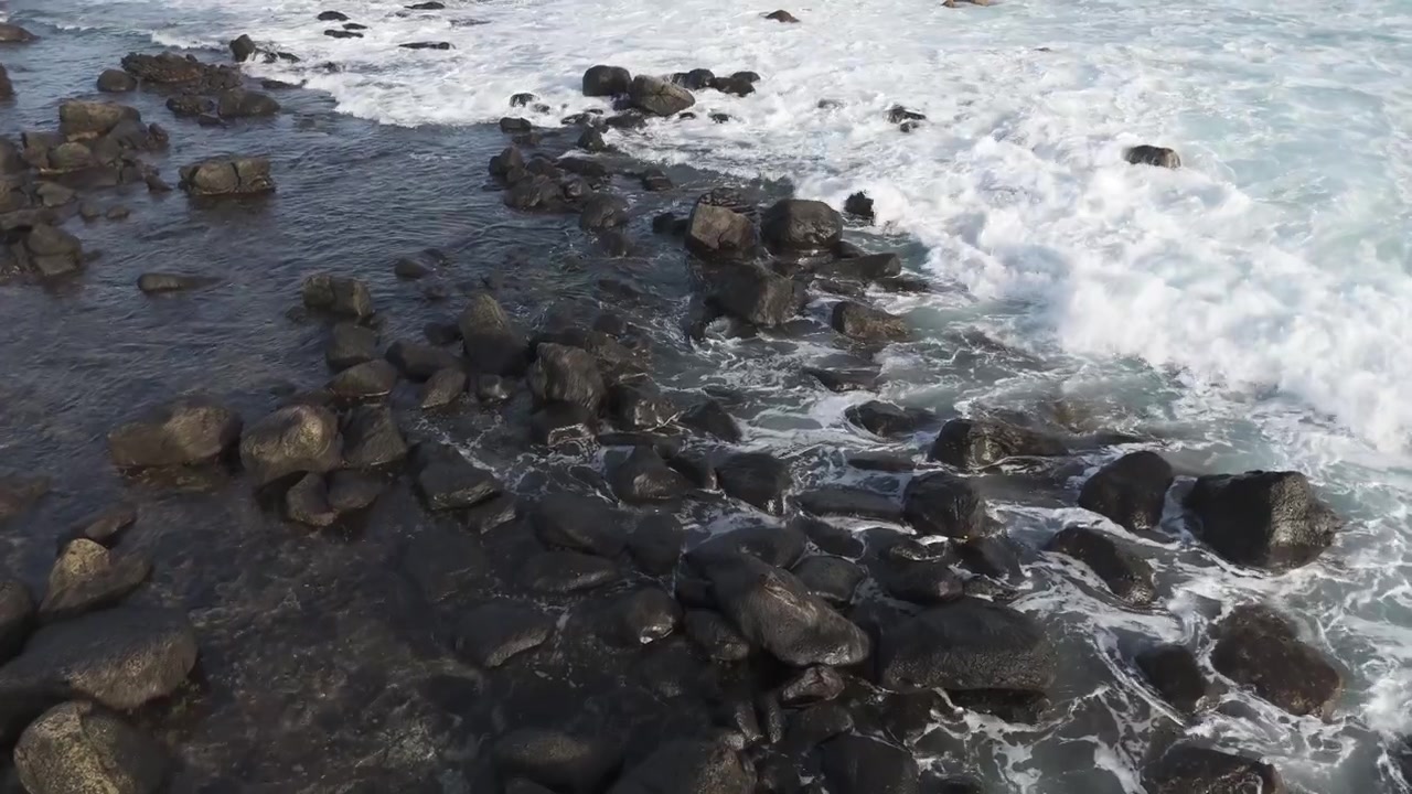 ランサローテ島の海岸で、大きな暗い火山岩の周りに泡立つ海水が押し寄せている。空撮、斜め上からのクローズアップ、自然の背景。