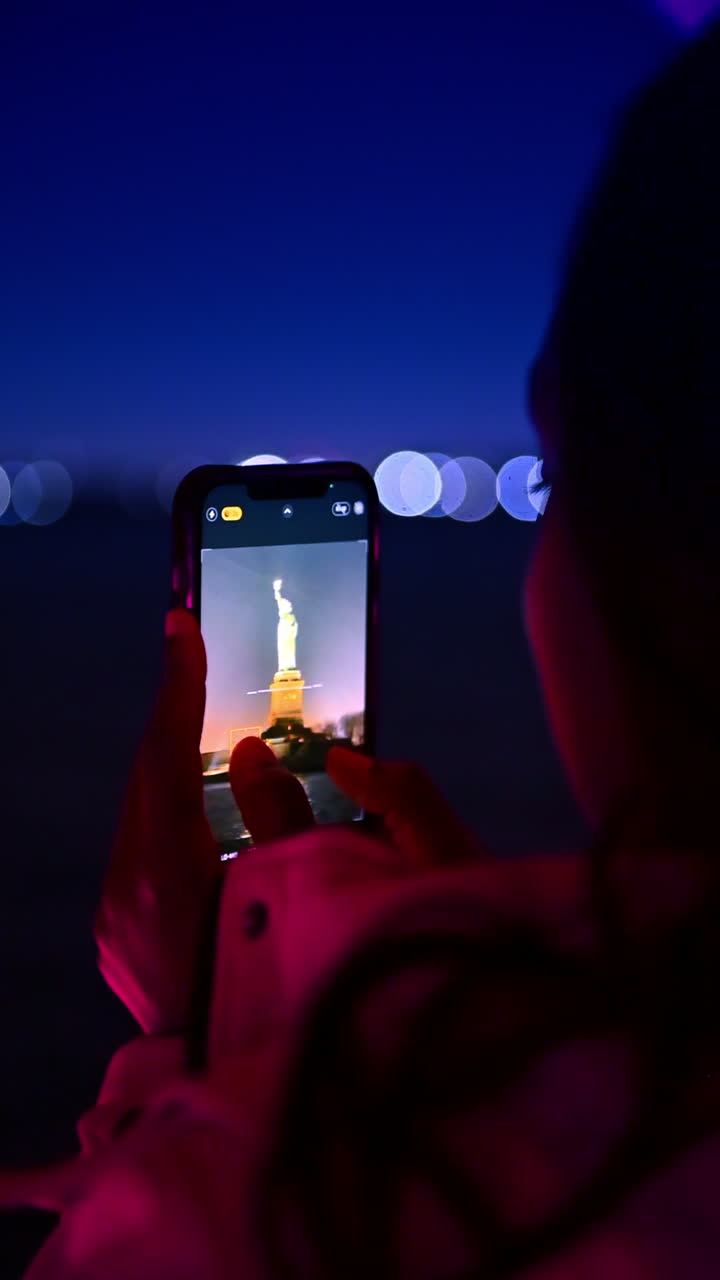 New York, USA, 8 agosto 2025: Mano che tiene uno smartphone e scatta una foto della Statua della Libertà. Primo piano dello schermo del telefono cellulare che riprende la Statua della Libertà di notte.