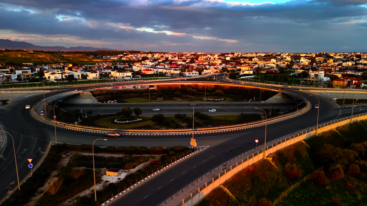 A stunning view of a winding road at sunset, surrounded by fields and a peaceful town. The warm light reflects off the landscapes, creating a serene atmosphere