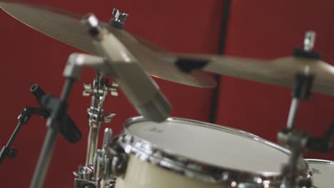 a vintage large diaphragm condenser microphone placed over a tom drum in a recording studio with another microphone in the background