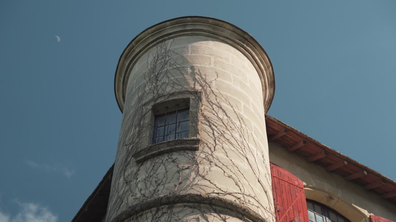 retrato de una torre de una casa antigua e histórica con ramas en las paredes, una ventana, luego otra con persianas rojas, un cielo azul con pocas nubes