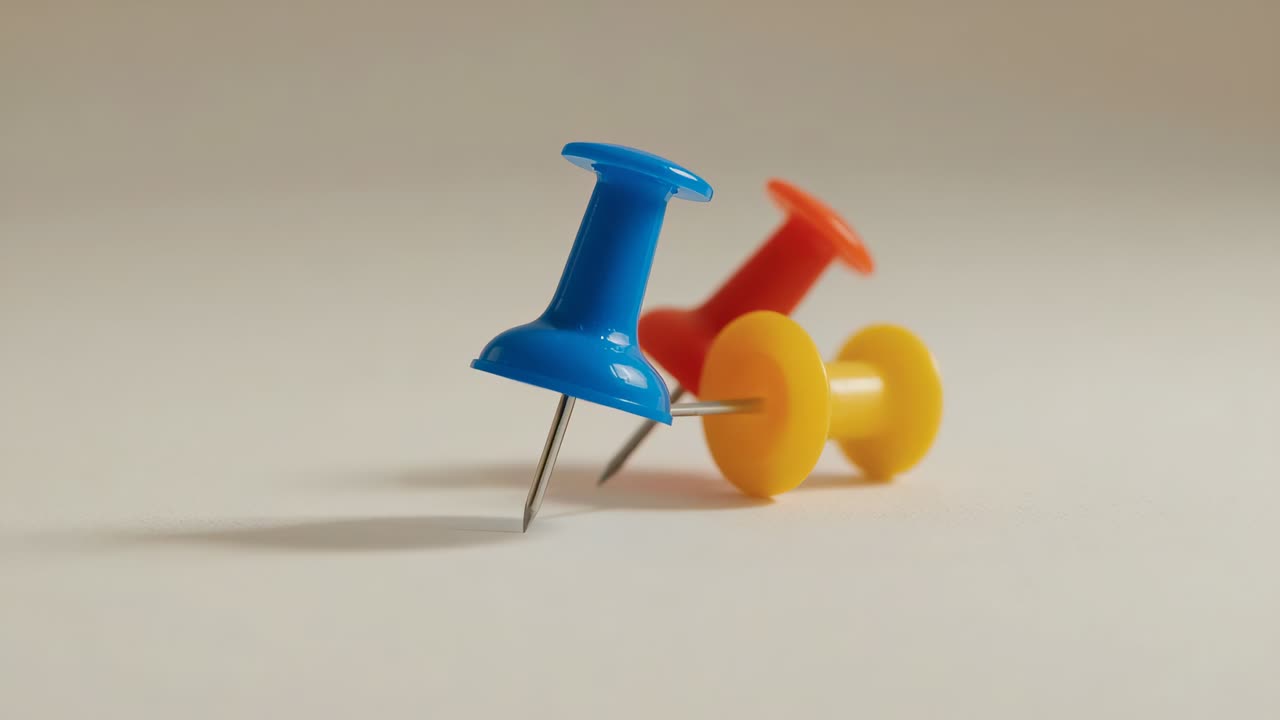 Showing blue orange and yellow push pins resting on smooth beige tabletop with blurred backdrop
