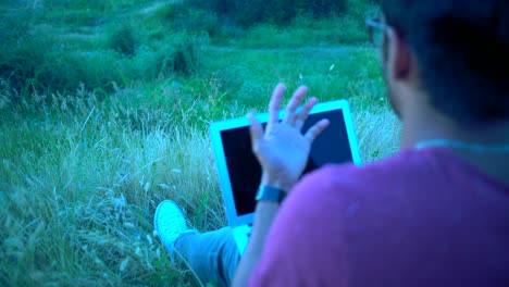 primer plano, reflejo en la pantalla del portátil, hombre indio hablando emocionalmente por teléfono arrodillado portátil sentado por la noche en la hierba en la colina de la cumbre
