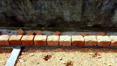 brick is laid, building the foundation of the house, workers work at a construction site in india, building a house with red stone , works using cement