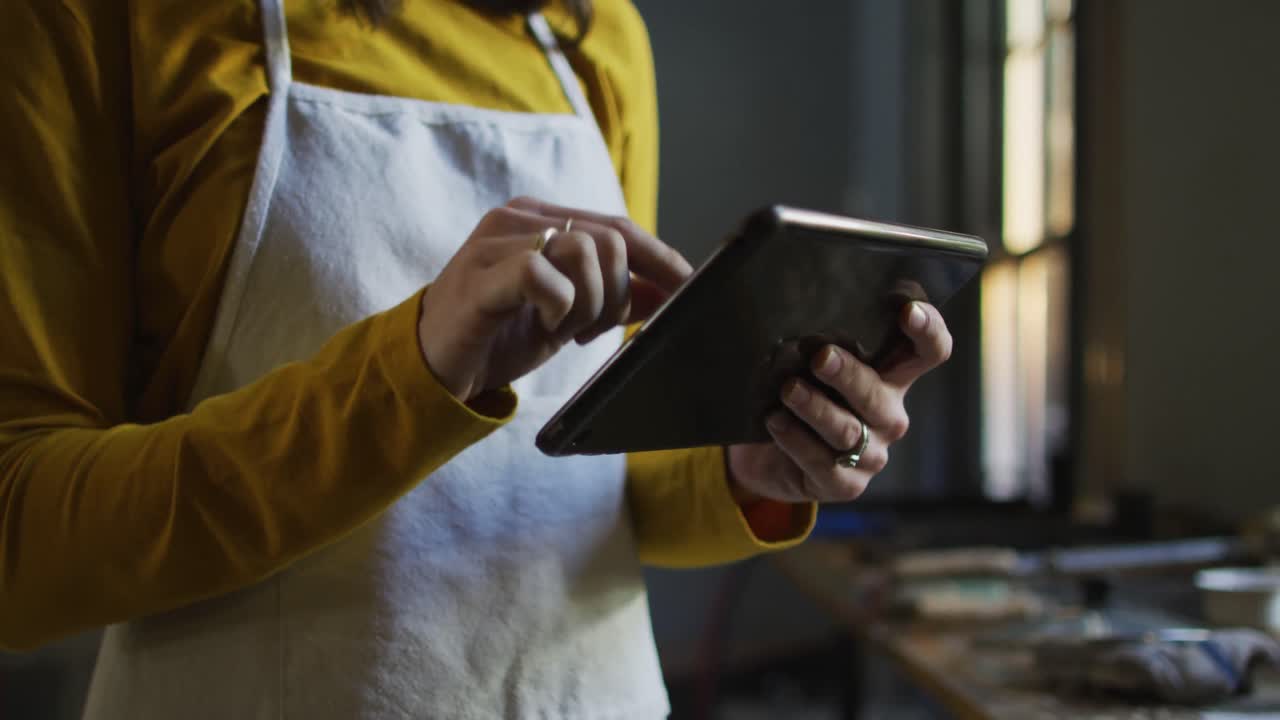 sección media de una joyera caucásica en un taller con un delantal, usando una tableta