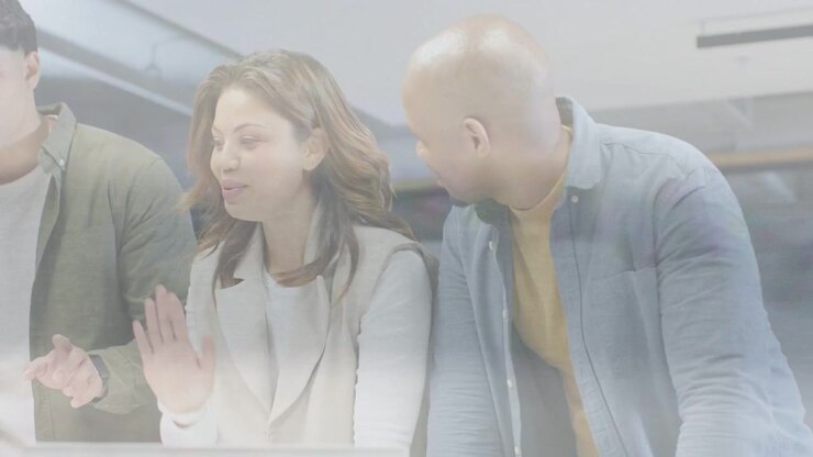 Business colleagues leaning in at desk, right colleague pointing at laptop and reviewing project