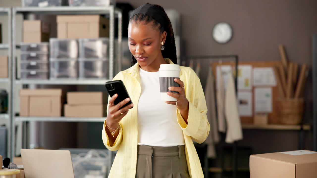 Giovane Donna di Colore che Beve Caffè e Usa il Telefono in un Ufficio di una Piccola Attività