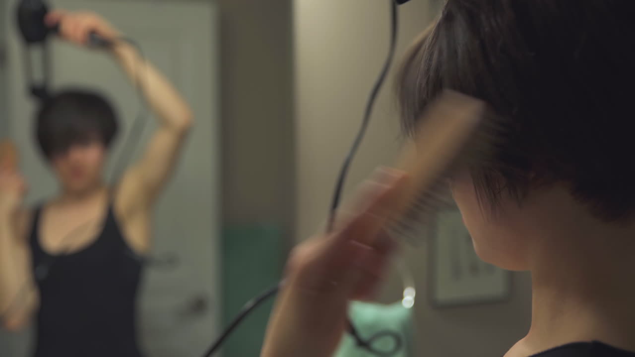 Mujer secándose y cepillándose el pelo mientras se mira al espejo