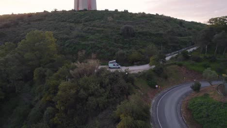 green roadsurfer travel camper van at the base of cristo rei, the sanctuary of christ the king, during early morning sunrise in lisbon portugal - aerial revers dolly pan raise