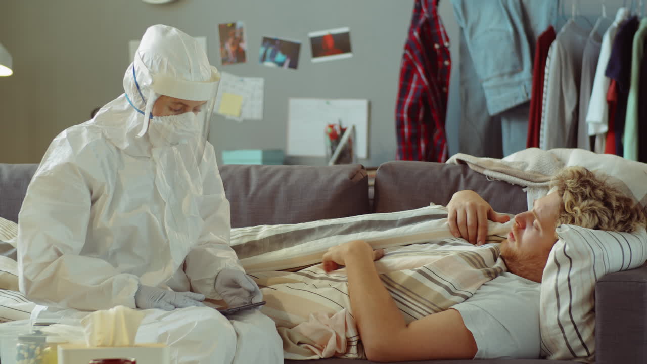 보호복을 입은 의사가 집에서 코로나 환자와 대화하고 있습니다.
