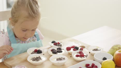 Girl-putting-berries-on-muffins-on-table