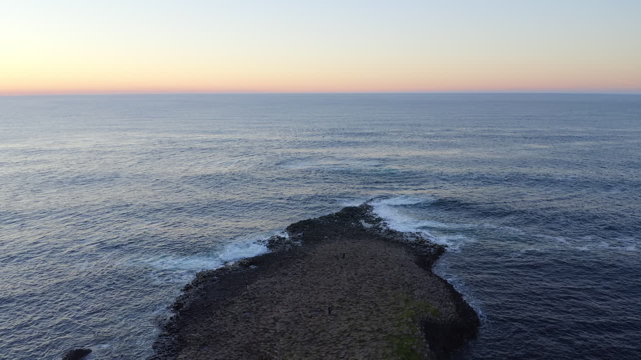 Static aerial of Giant’s Causeway basalt formations in the foreground, with a calm sea horizon and warm sunset