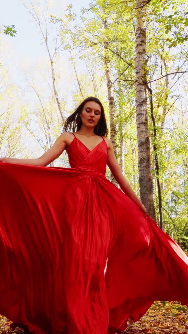 Enchanting Beauty in Nature: A Stunning Model Dressed in a Flowing Red Dress Captured Amidst a Serene Woodland Background with Autumn Foliage