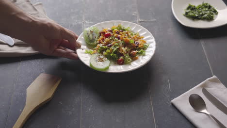 man's hand puts salad with fruits and vegetables on table