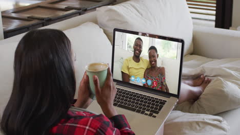 mujer afroamericana sosteniendo una taza de café haciendo una videollamada en una computadora portátil sentada en el sofá en casa