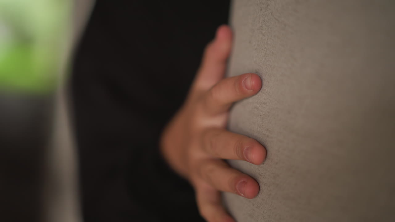 Mano su un pilastro di cemento bagnato in un sottopassaggio urbano piovoso. Primo piano delle dita che afferrano una superficie ruvida, con sfondo bokeh morbido, luce suggestiva, posa di riparo, sottili gocce di pioggia e riflessi nelle pozzanghere.