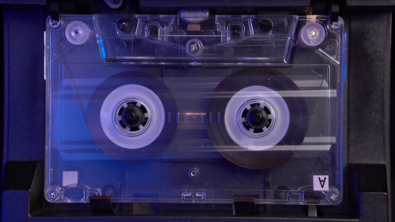 tocando cintas de cassette de audio transparentes en el reproductor de la cubierta de los años 80, rodillos giratorios, primer plano
