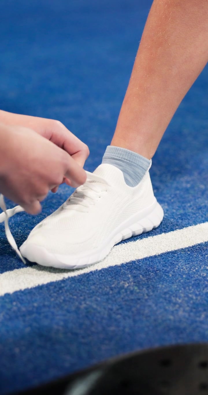 Persona che allaccia i lacci di una scarpa da ginnastica bianca su un campo da padel blu