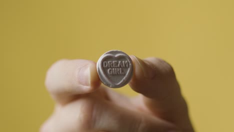 primer plano de la mano que sostiene el caramelo del corazón con el mensaje de la chica de los sueños sobre fondo amarillo